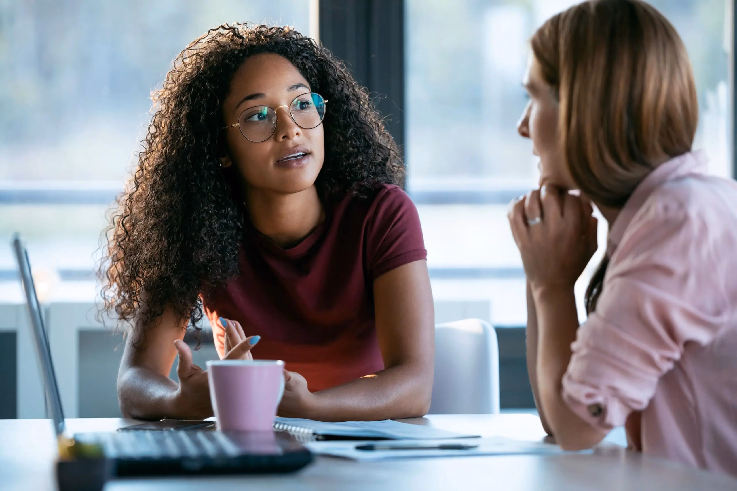 Woman in glasses and a red shirt talking with her coworker in the office
