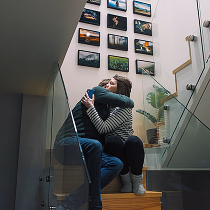 man and woman sit on stairs comforting each other by hugging