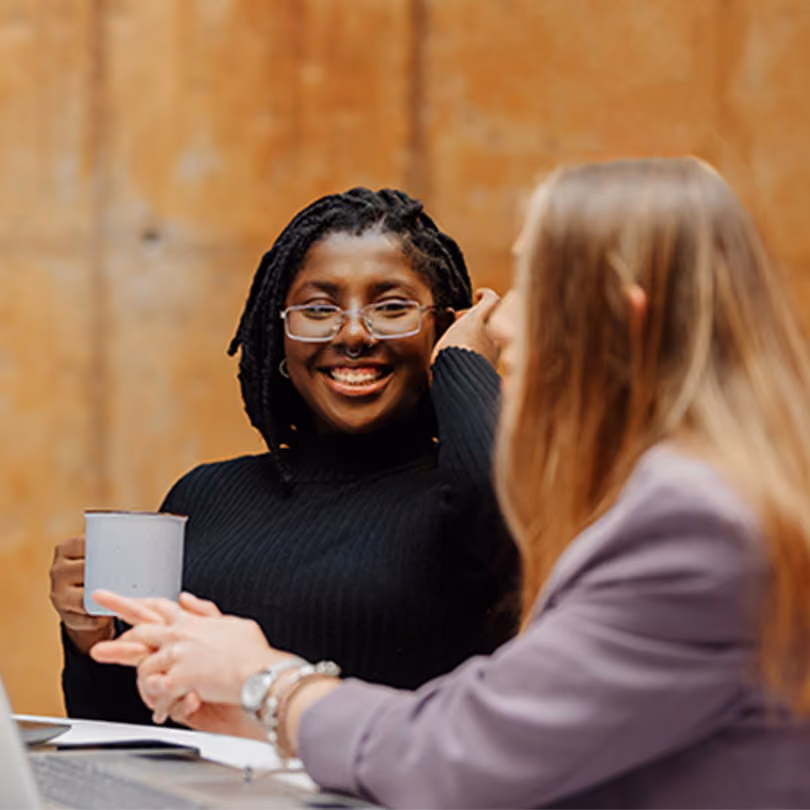 Woman with glasses and a septum piercing smiling and talking to her colleague