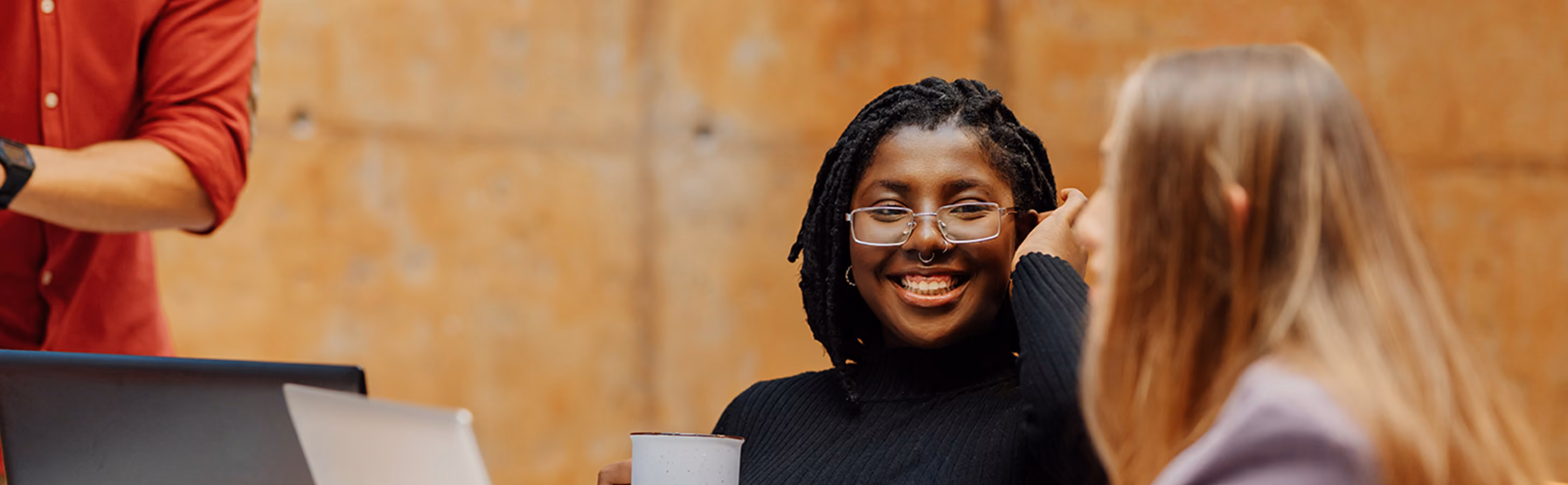Woman with glasses and a septum piercing smiling and talking to her colleague