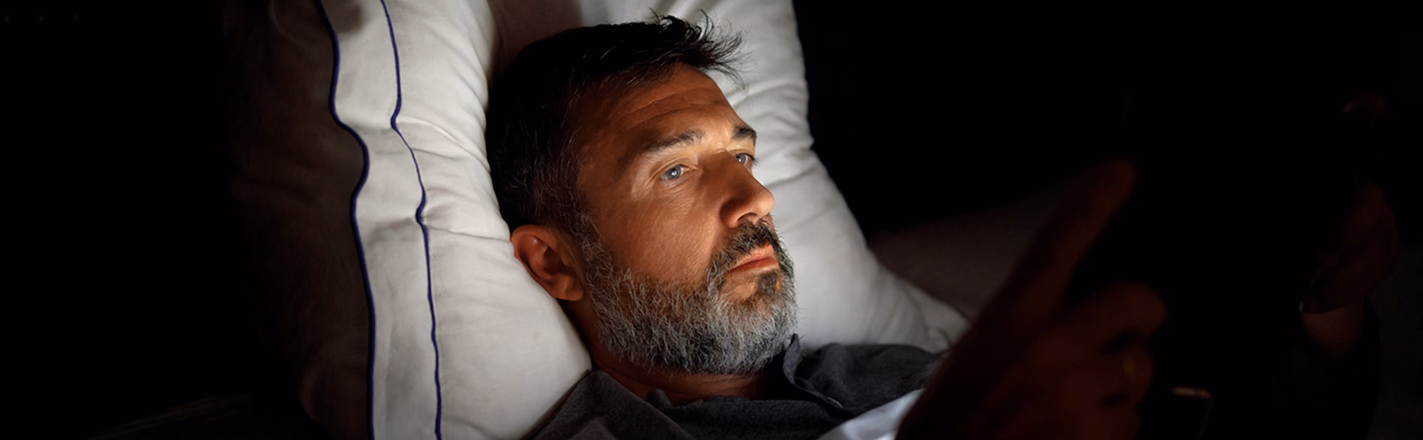 Man laying in his bed in the dark looking at his phone