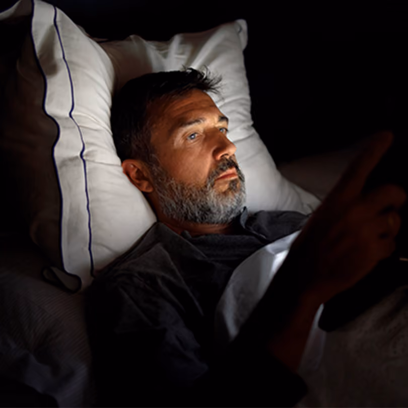 Man laying in his bed in the dark looking at his phone