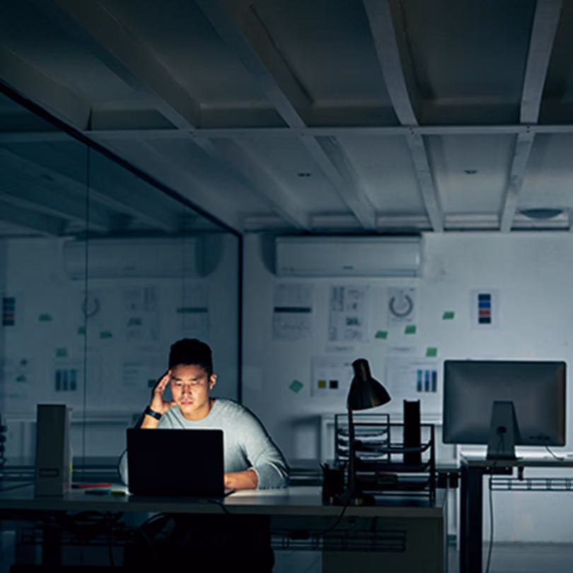 A stressed man sits at his desk in the dark at the office