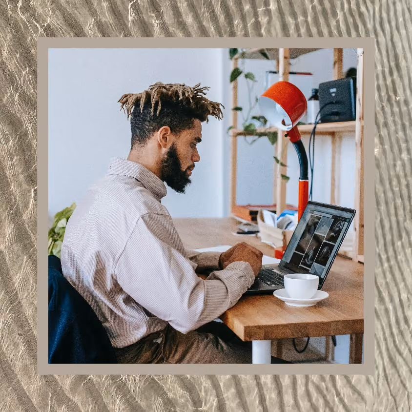 A man works on his computer at his desk with a cup of coffee