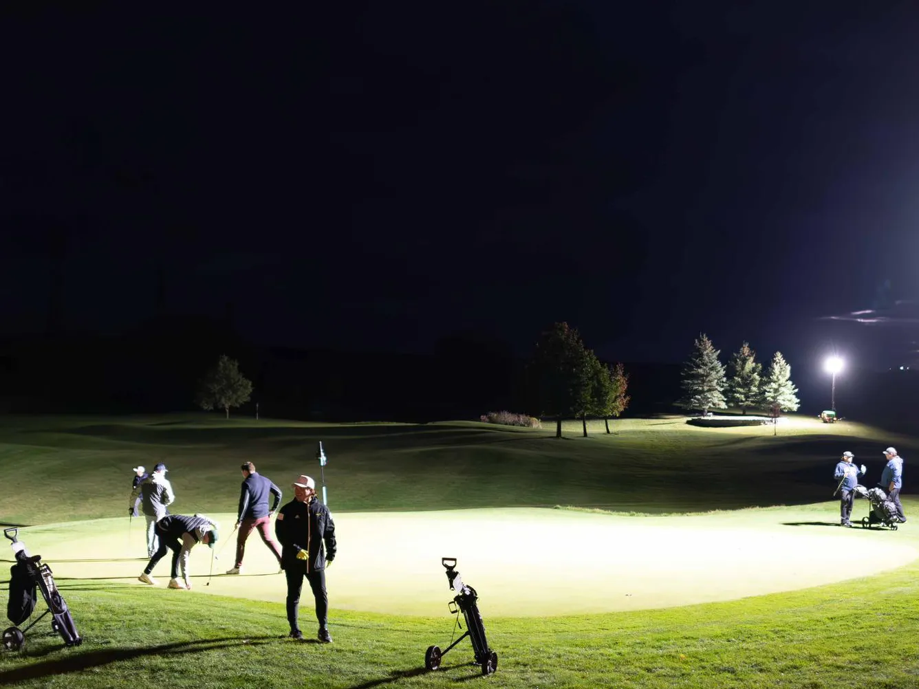 Several golfers take position on the green during a night time golf game at The Badlands.