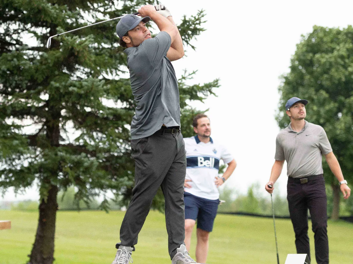 A golfer tees off while two other golfer watch the ball take flight.