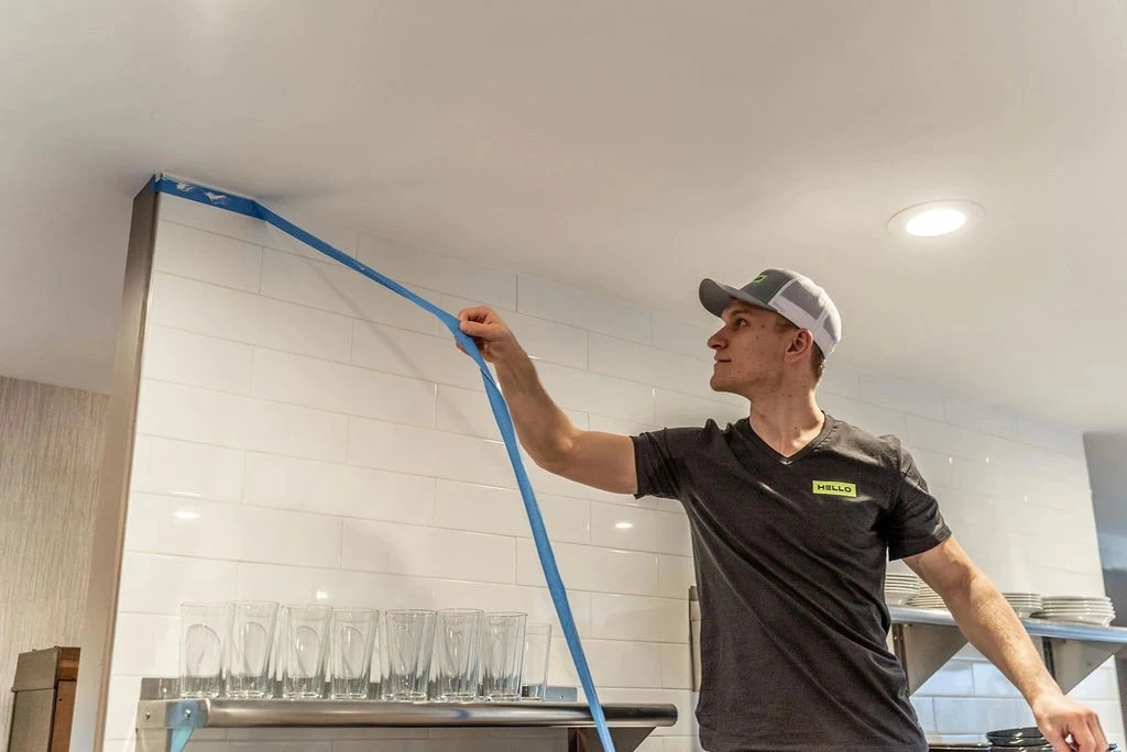 HELLO Painting professional pulling painter's tape along a ceiling edge in a Bellevue kitchen