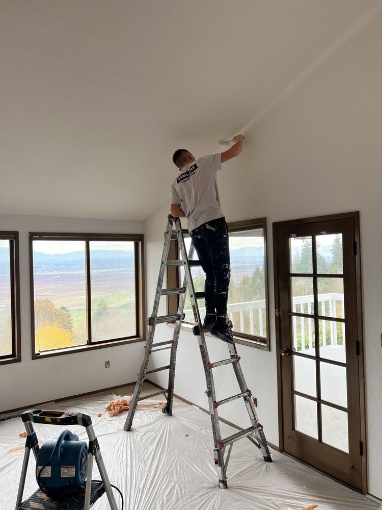 A Hello Painting contractor atop a foldable ladder while working on a drywall repair in a Bellevue home