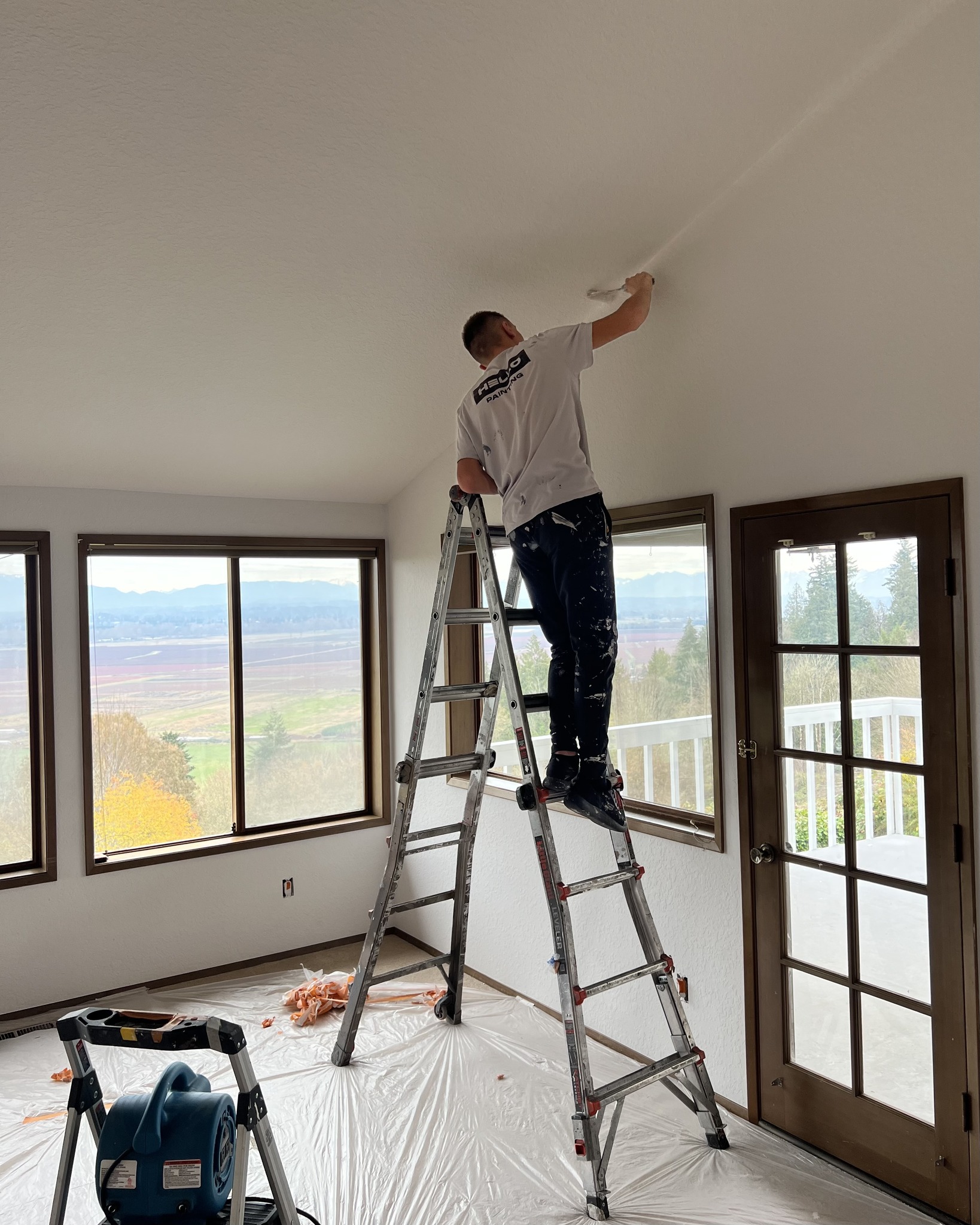 HELLO Painting painter applying interior ceiling paint while protecting floors and windows during a residential painting project