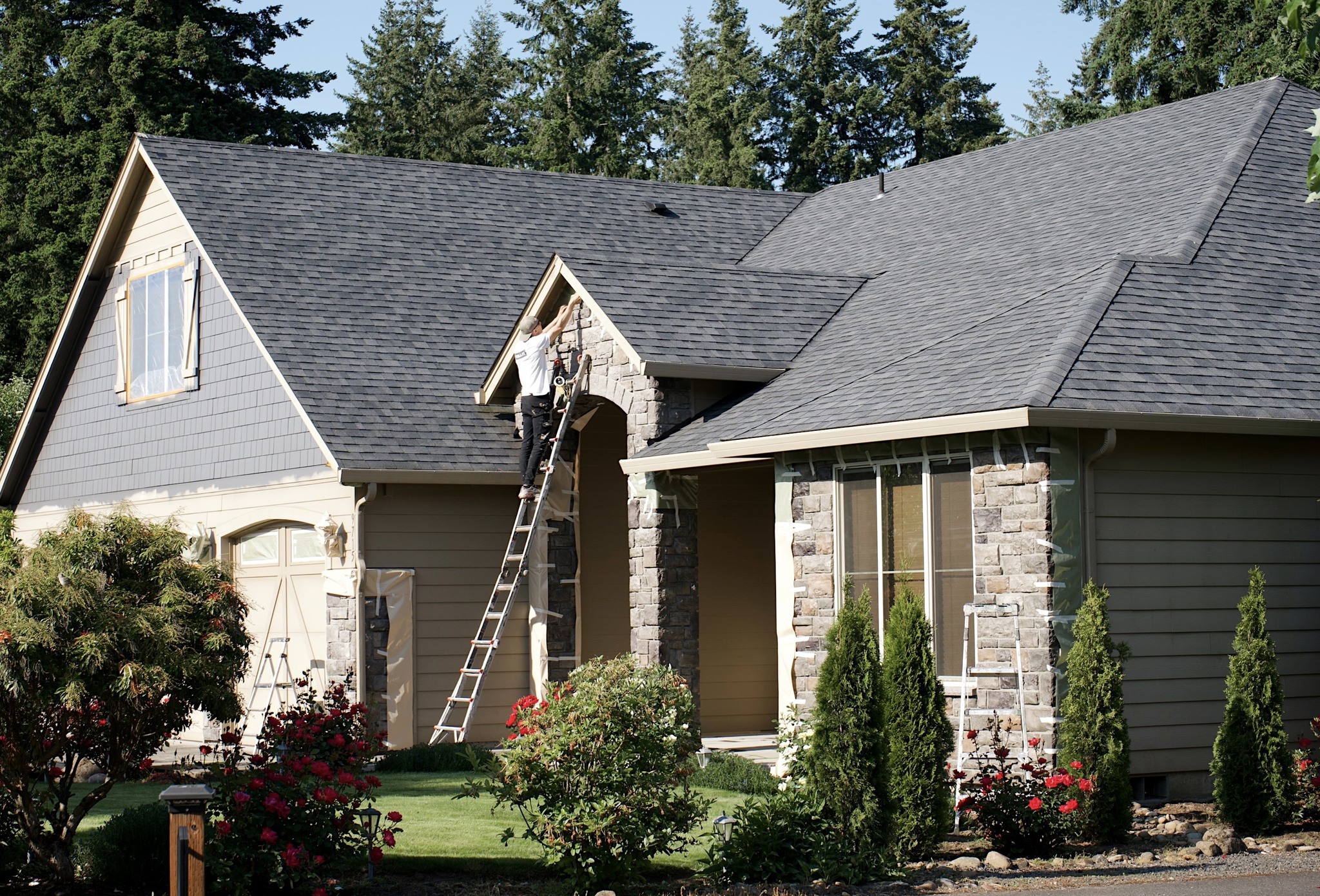 Exterior house painting in progress with a painter working on trim and siding from a ladder