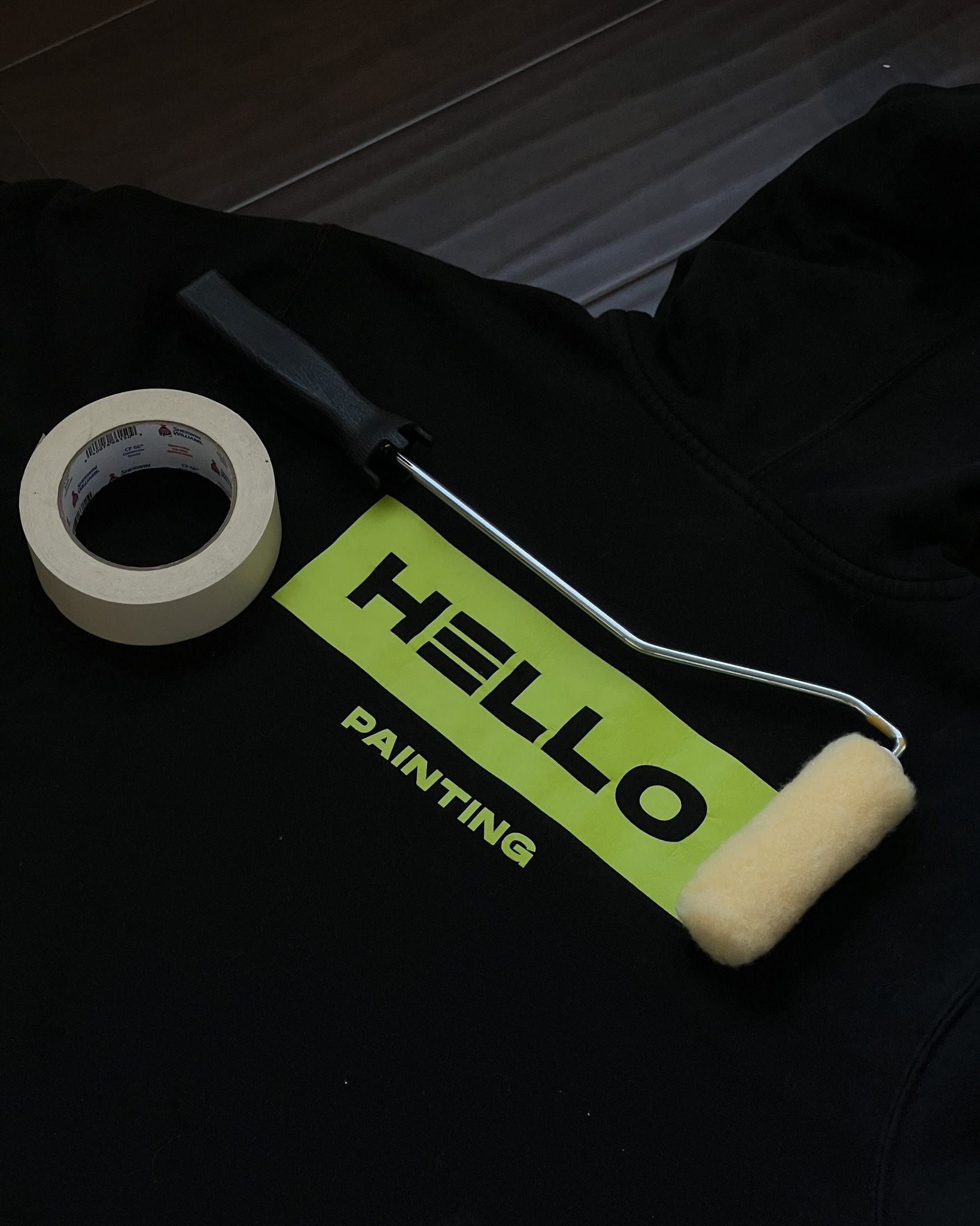 Painting tools including roller and tape placed on HELLO Painting branded hoodie