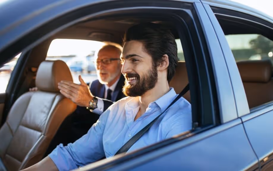 A smiling young man in the driver's seat of an ambulatory transport conversing with an older man in the backseat