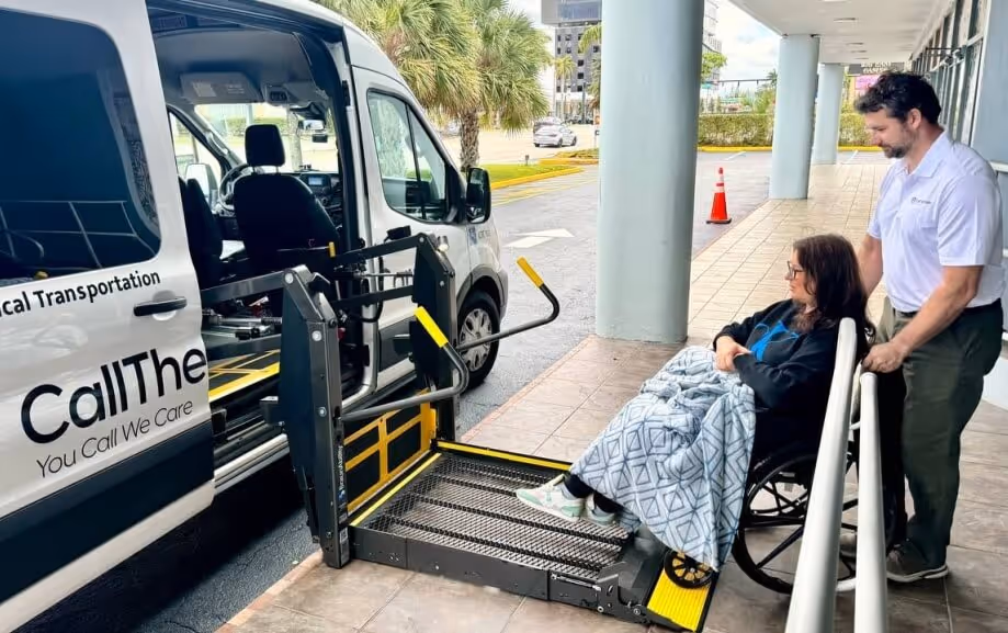 A woman in a wheelchair accessing an equipped wheelchair transport van with the assistance of service personnel