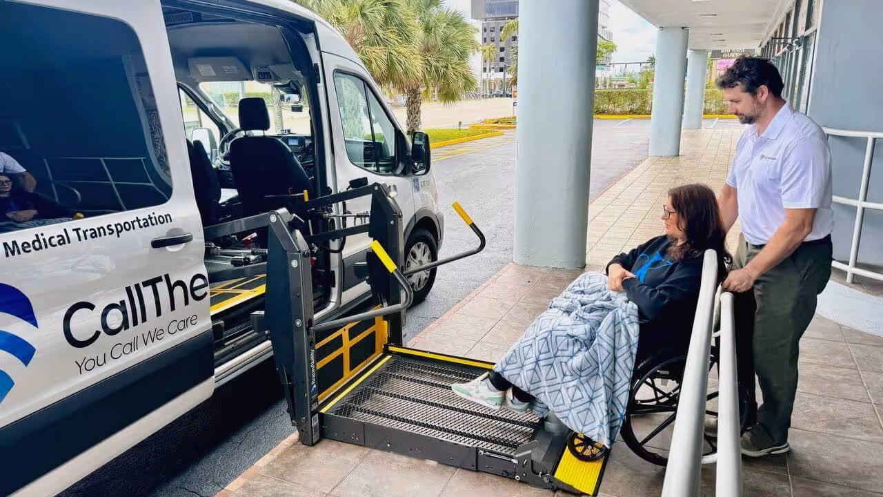 A woman in a wheelchair is being assisted by a man onto a wheelchair-accessible lift connected to a medical transportation van