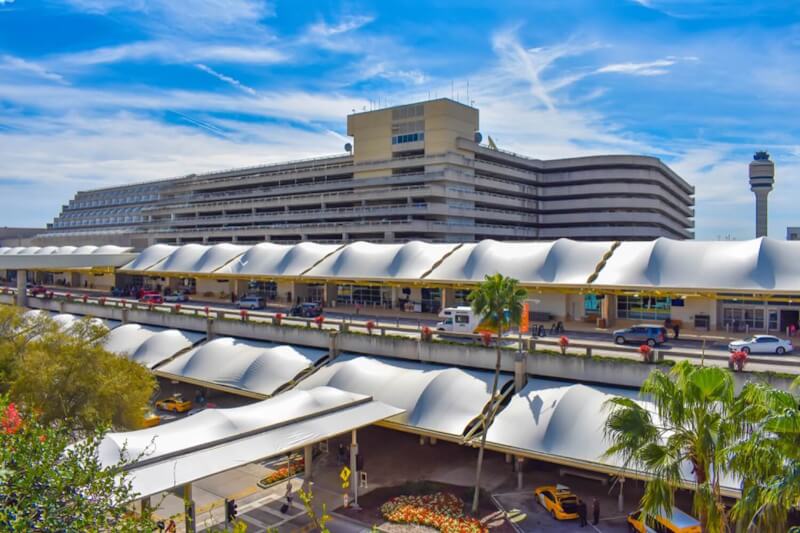 Panoramic view of Terminal A at Orlando International Airport with vehicles, palm trees, and control tower in the background.