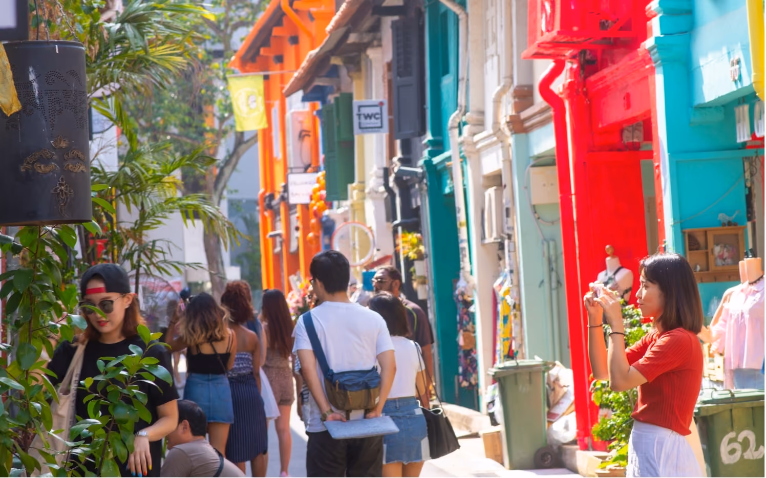 People walking and taking photos on a vibrant street lined with colorful buildings in red, turquoise, and orange shades.