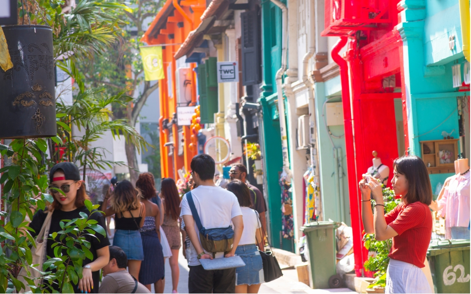 People walking and taking photos in a colorful street with brightly painted shopfronts in red, orange, yellow, and turquoise.