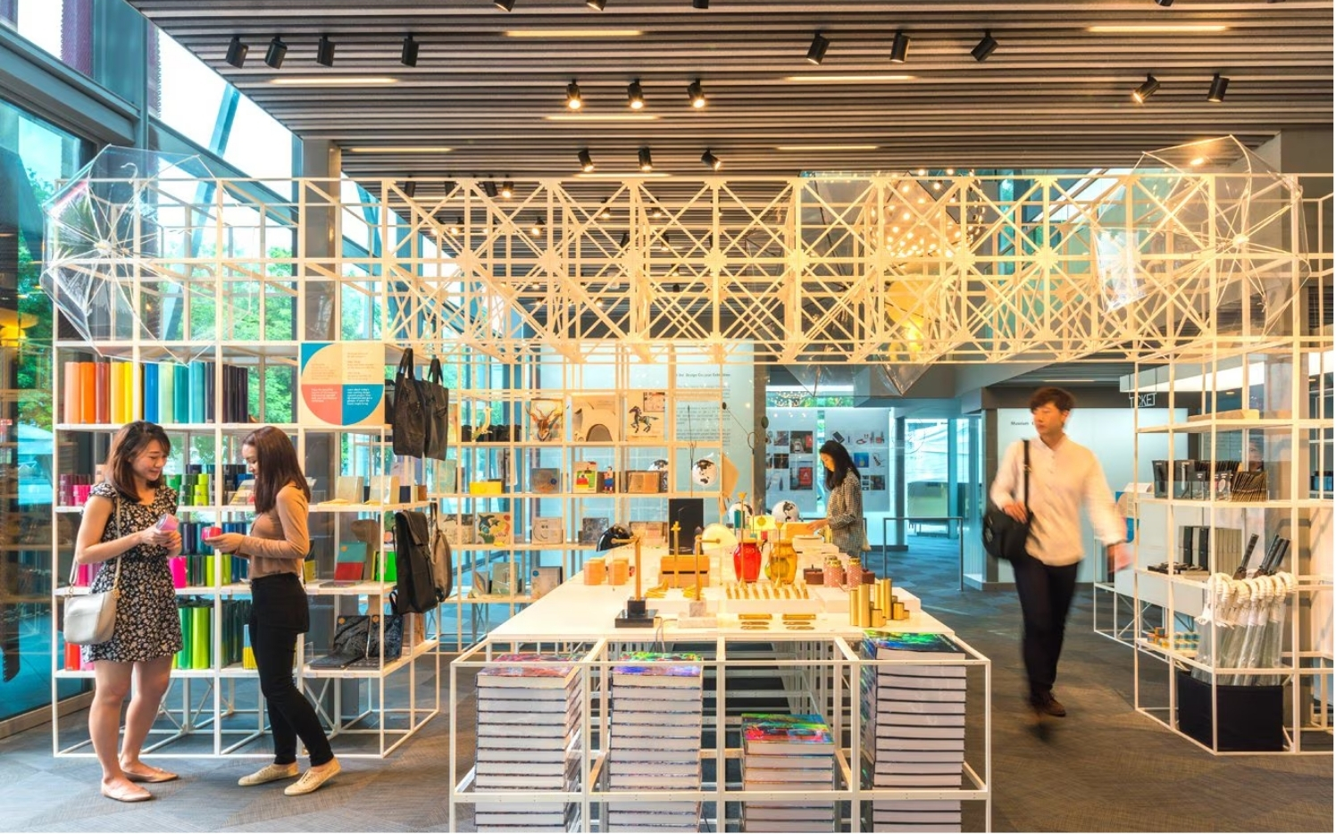 Interior of a modern store with colorful items on shelves, two women looking at products, and a man walking in the background.