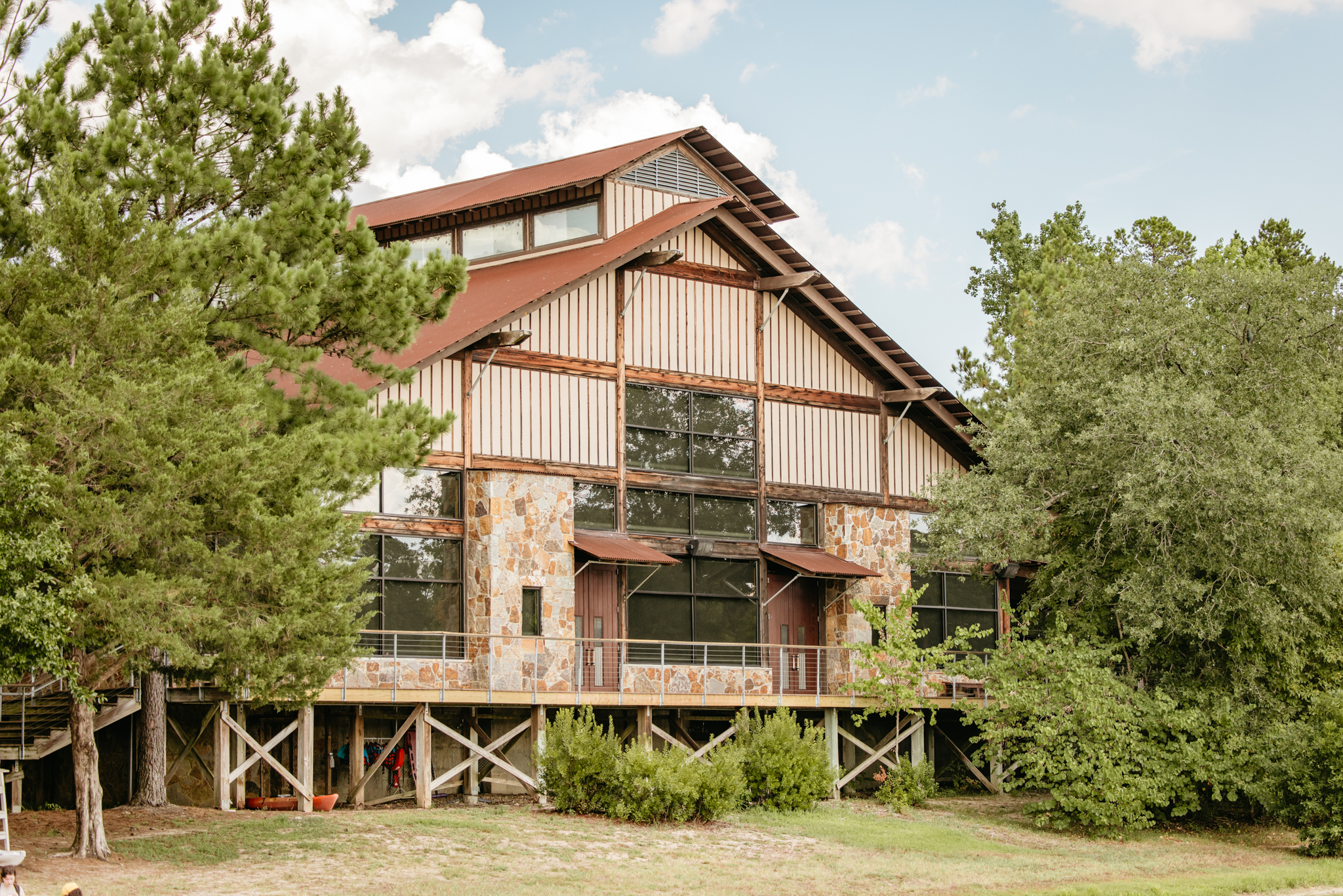 Large rustic building with stone and wood exterior surrounded by green trees under a partly cloudy sky.