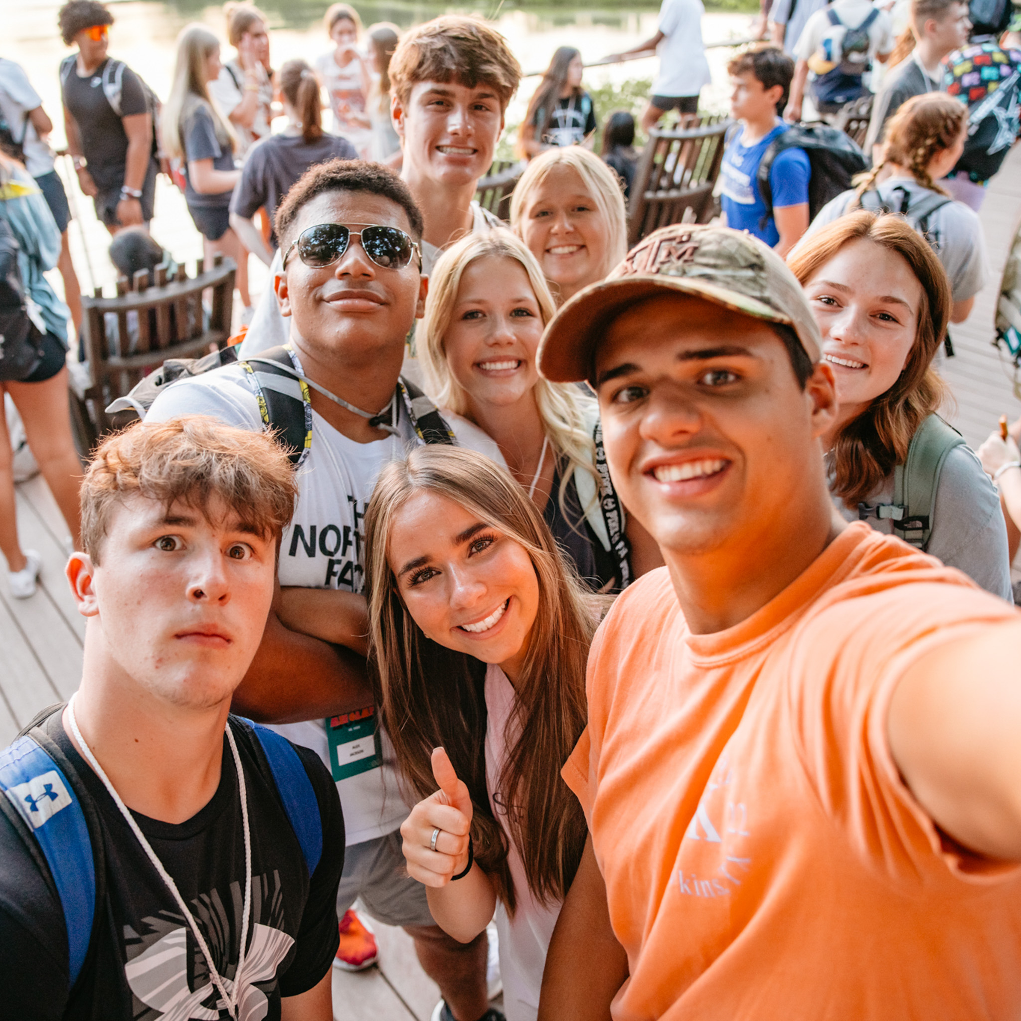 Group of smiling young people taking a selfie outdoors, with one woman giving a thumbs up.