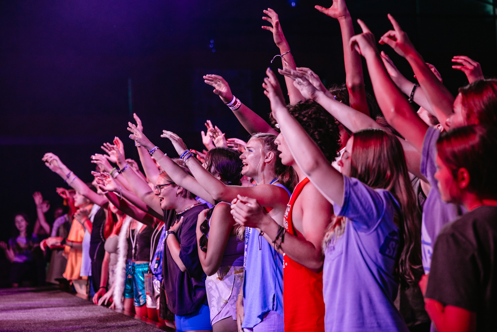 Group of young people standing close together with arms raised, engaging enthusiastically at an event.