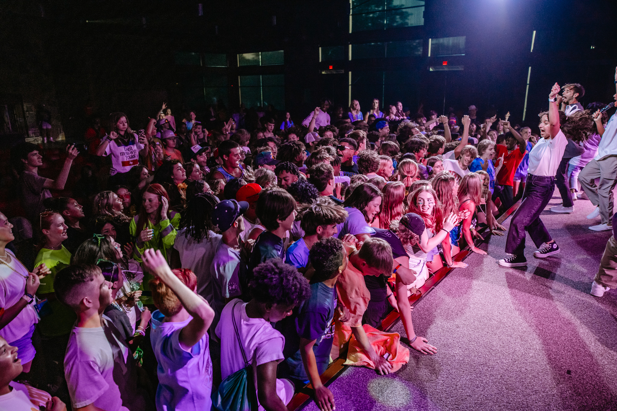 Excited crowd of young people enjoying a lively indoor concert with performers on stage.