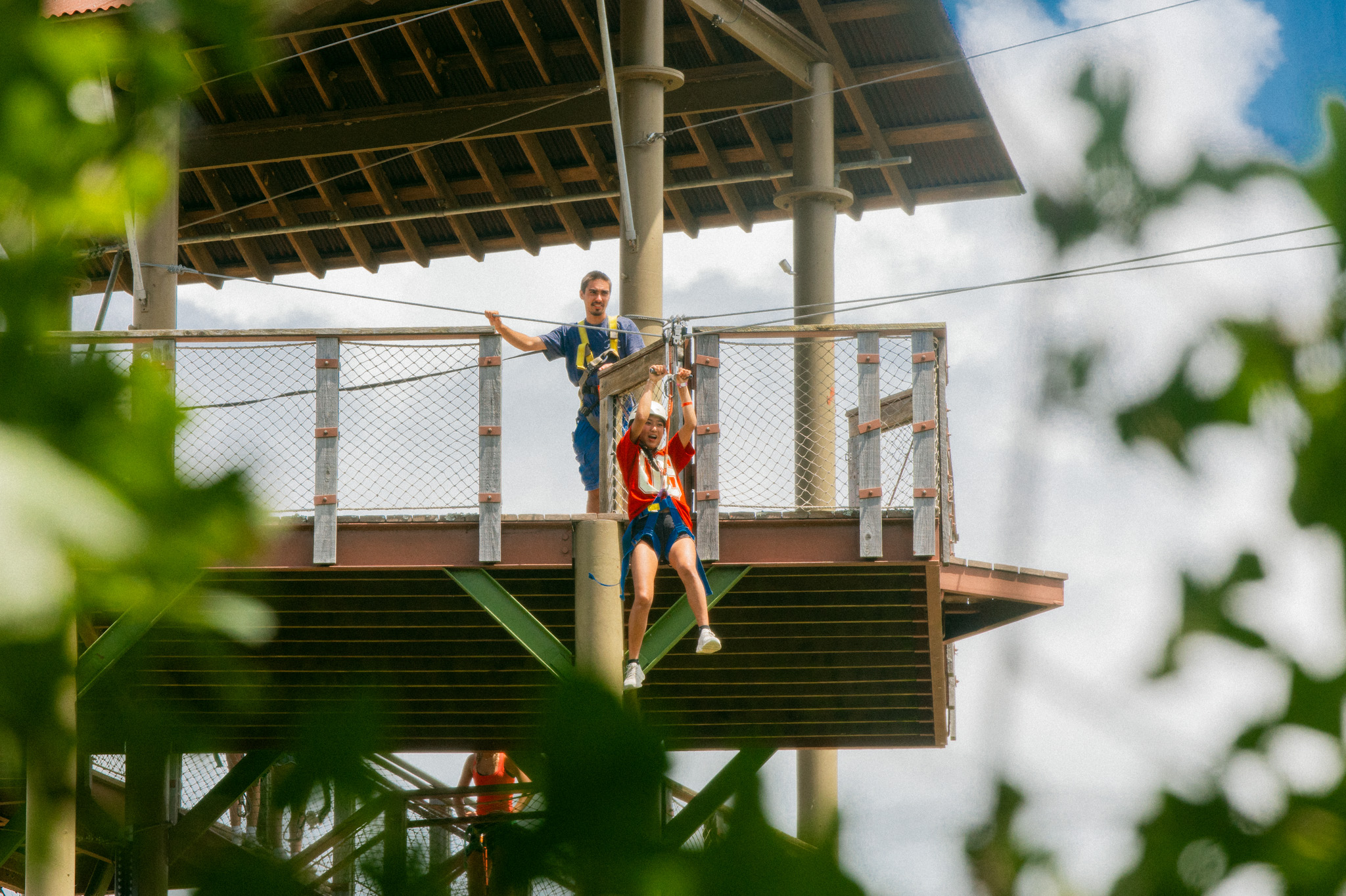 Person in red shirt riding a zipline from a platform with an instructor in blue behind them.