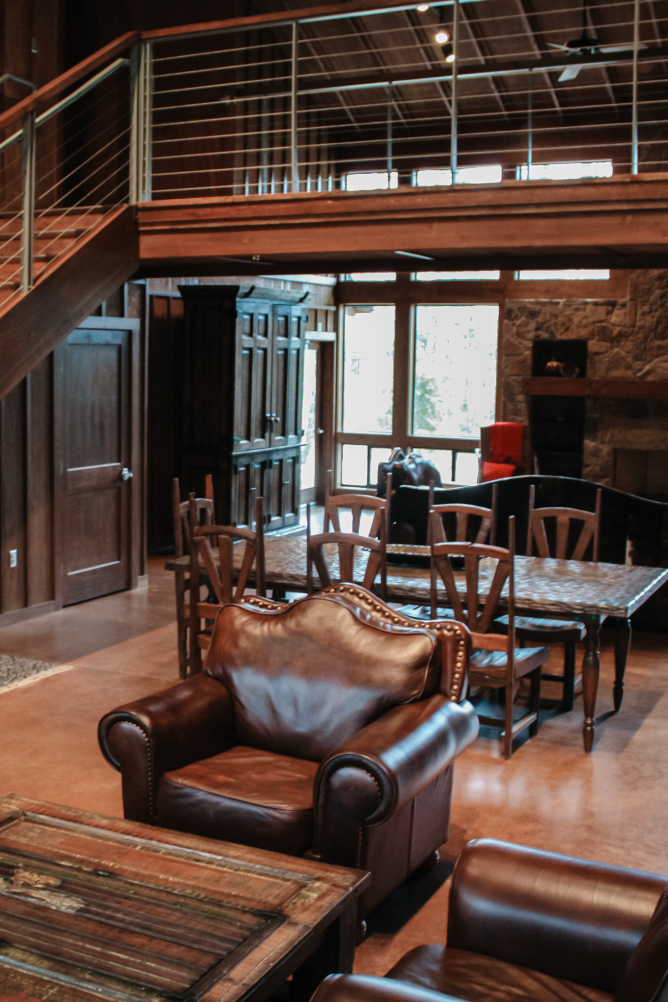 Rustic living room with brown leather armchairs, wooden coffee table, dining table with chairs, and large windows.