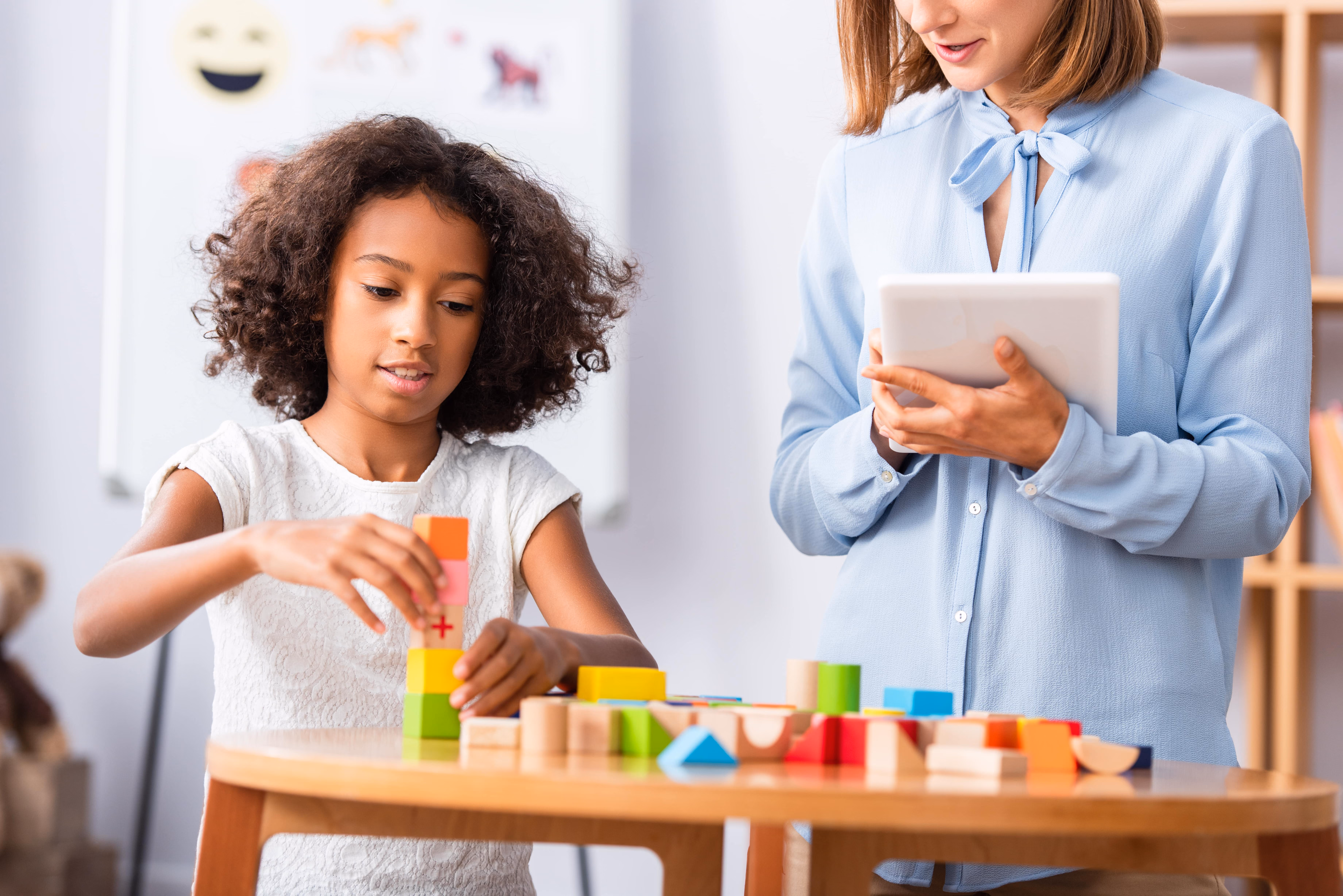 A young girl is building blocks while a therapist takes notes.