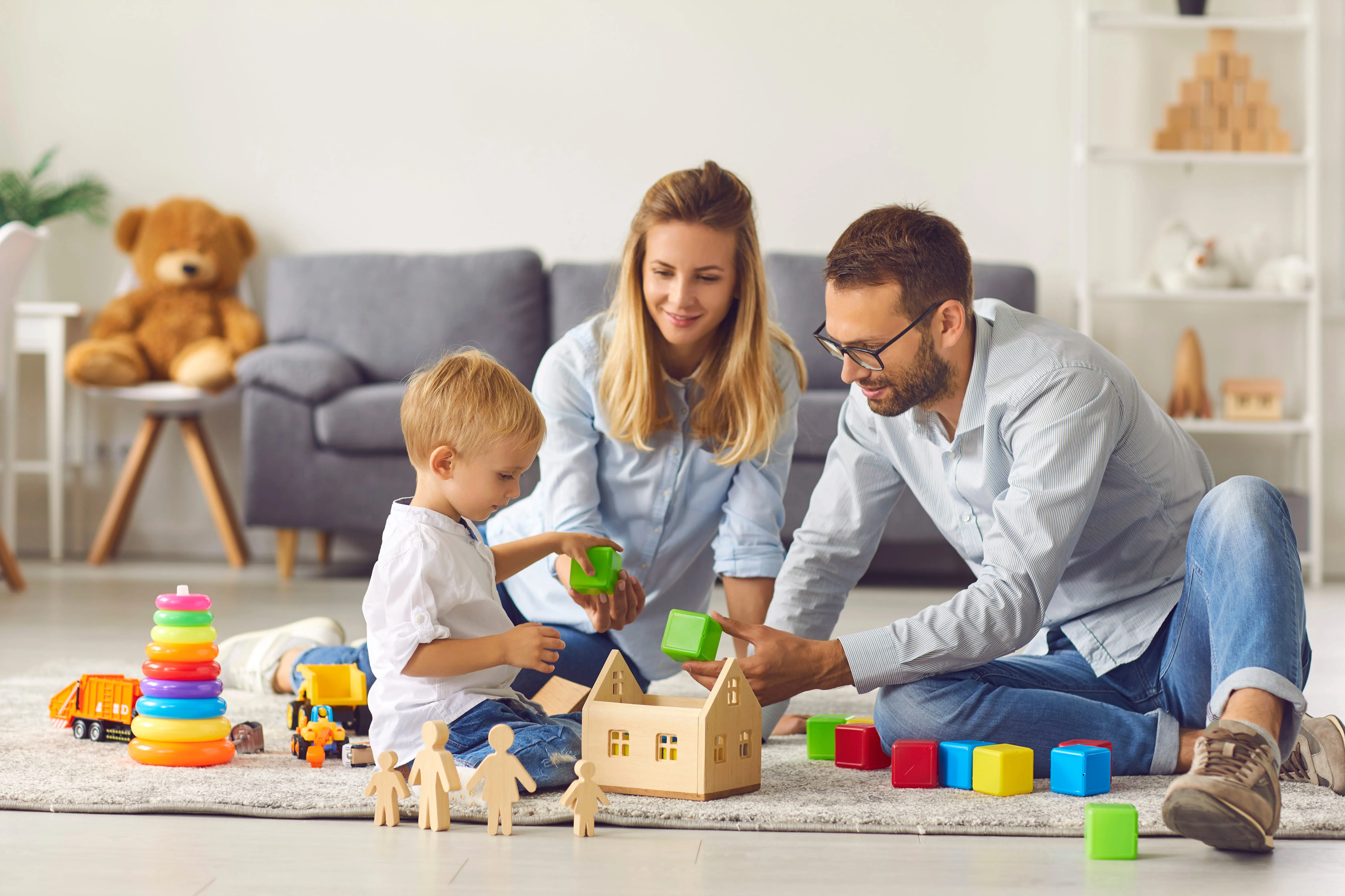 A father, mother, and toddler are playing with blocks in their home.