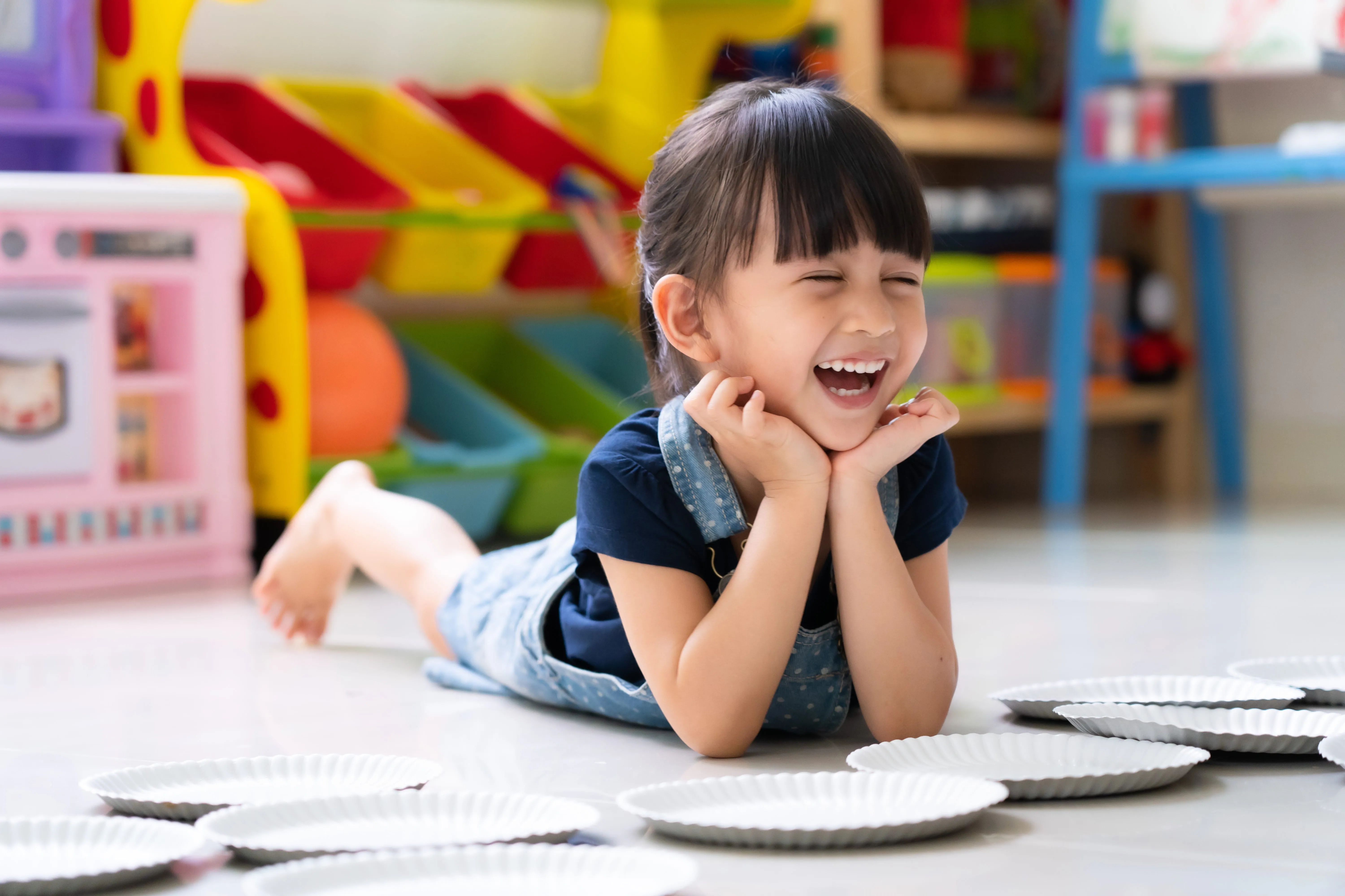 A little girl is laughing while laying on the floor playing.