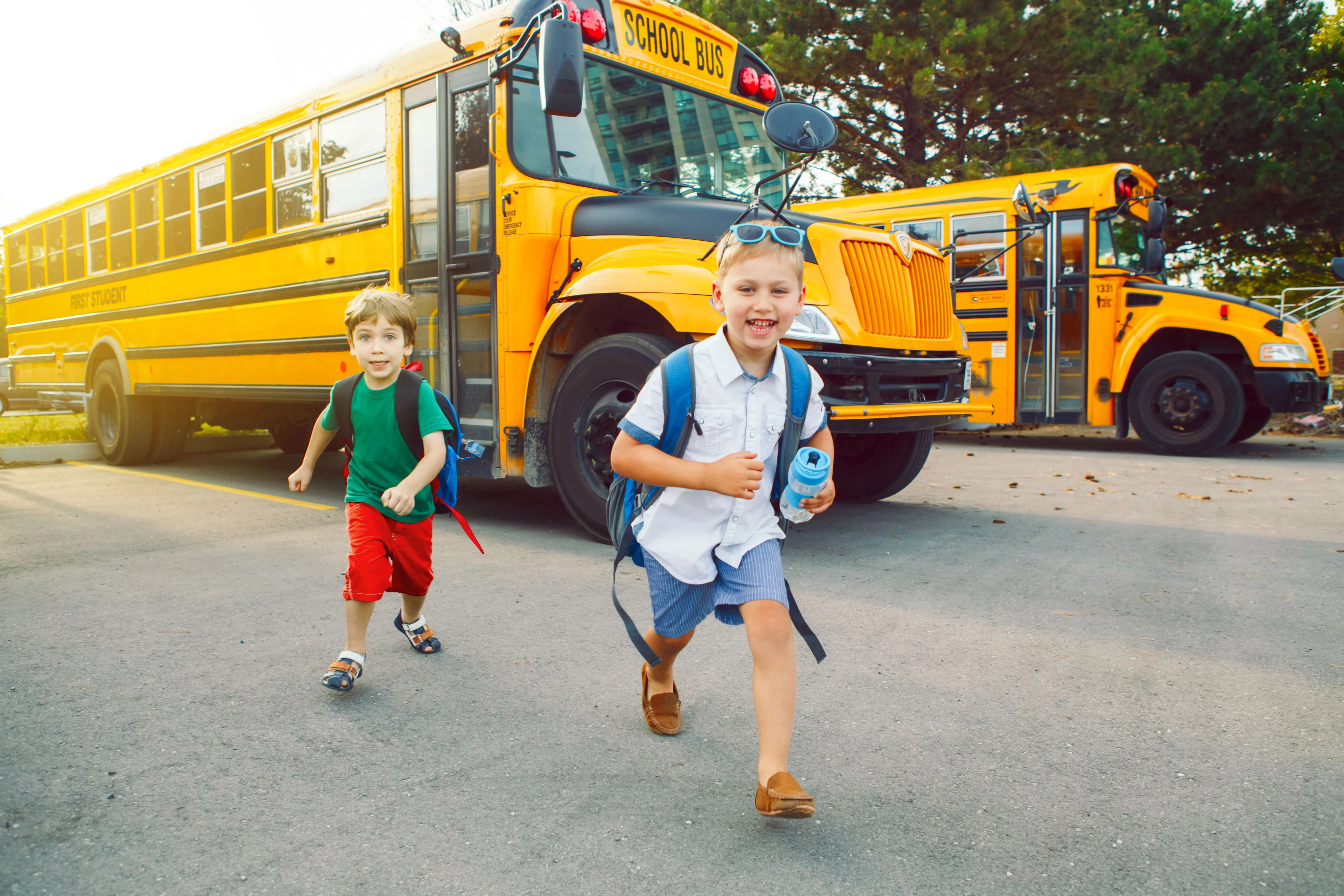 Two young boys running from the school bus excited for school.