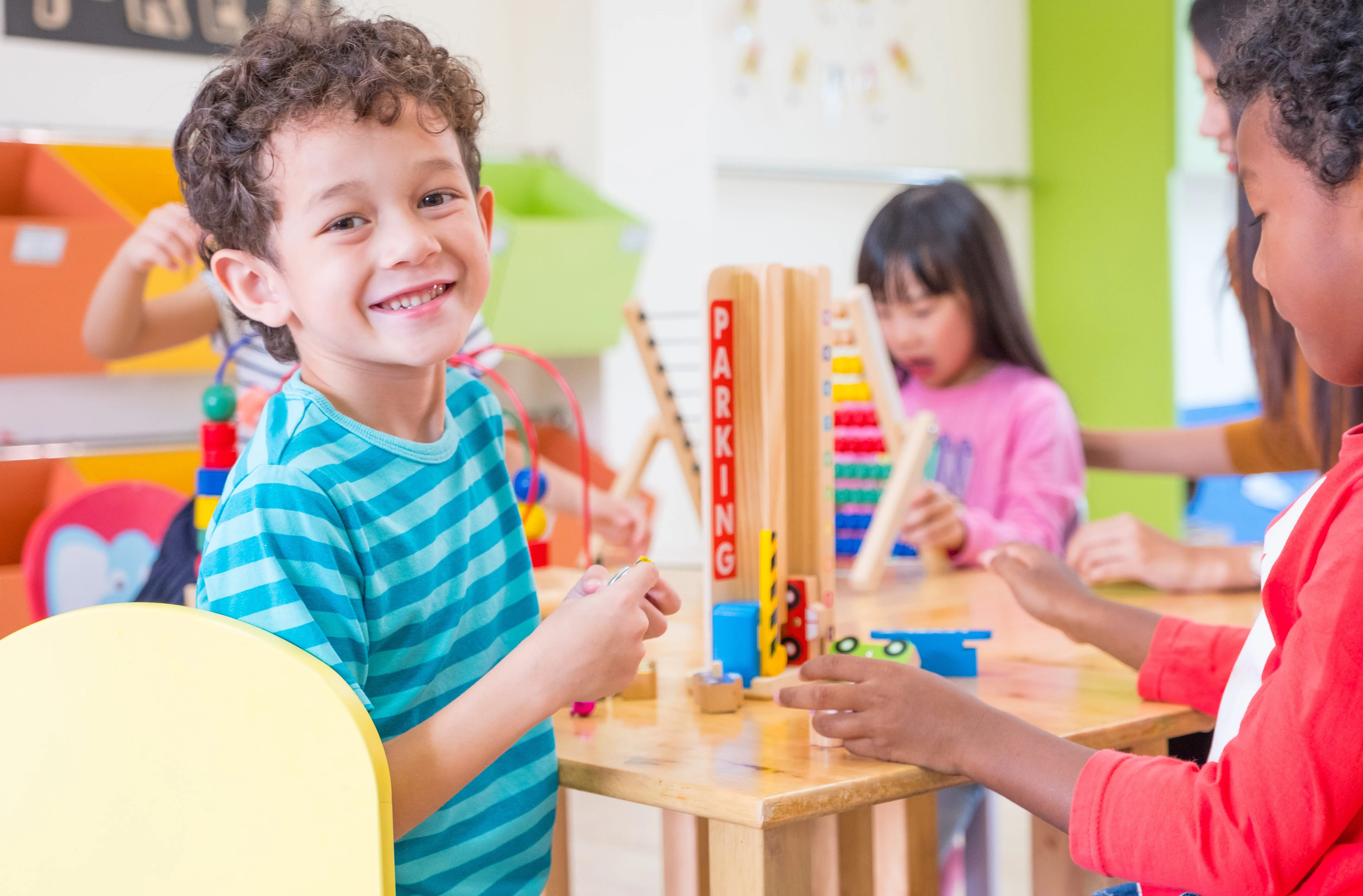 A young boy smiling as he plays in the classroom with a friend.