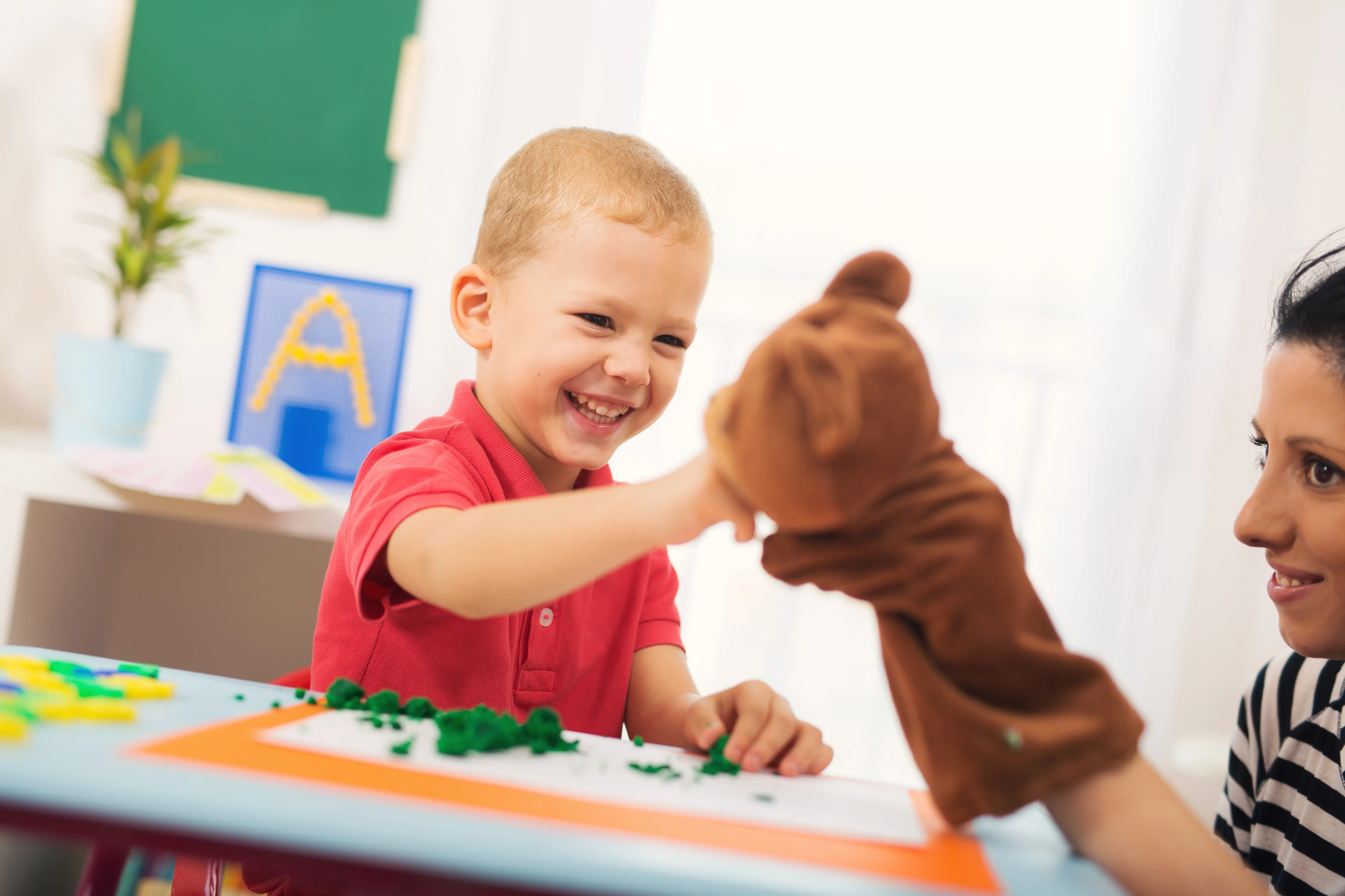 A young boy playing with a stuffed bear puppet.