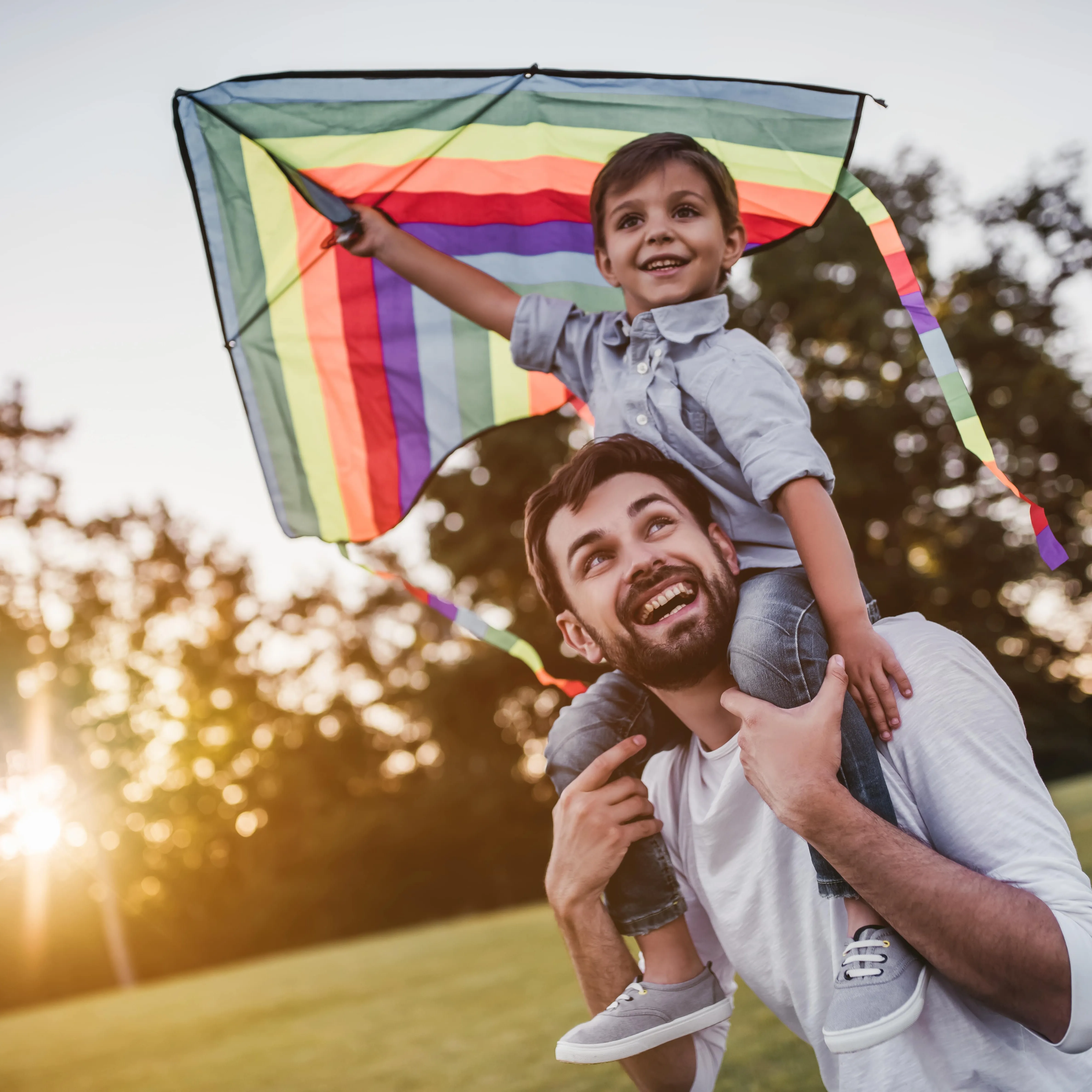 A father with his son on his shoulders who is holding a kite.