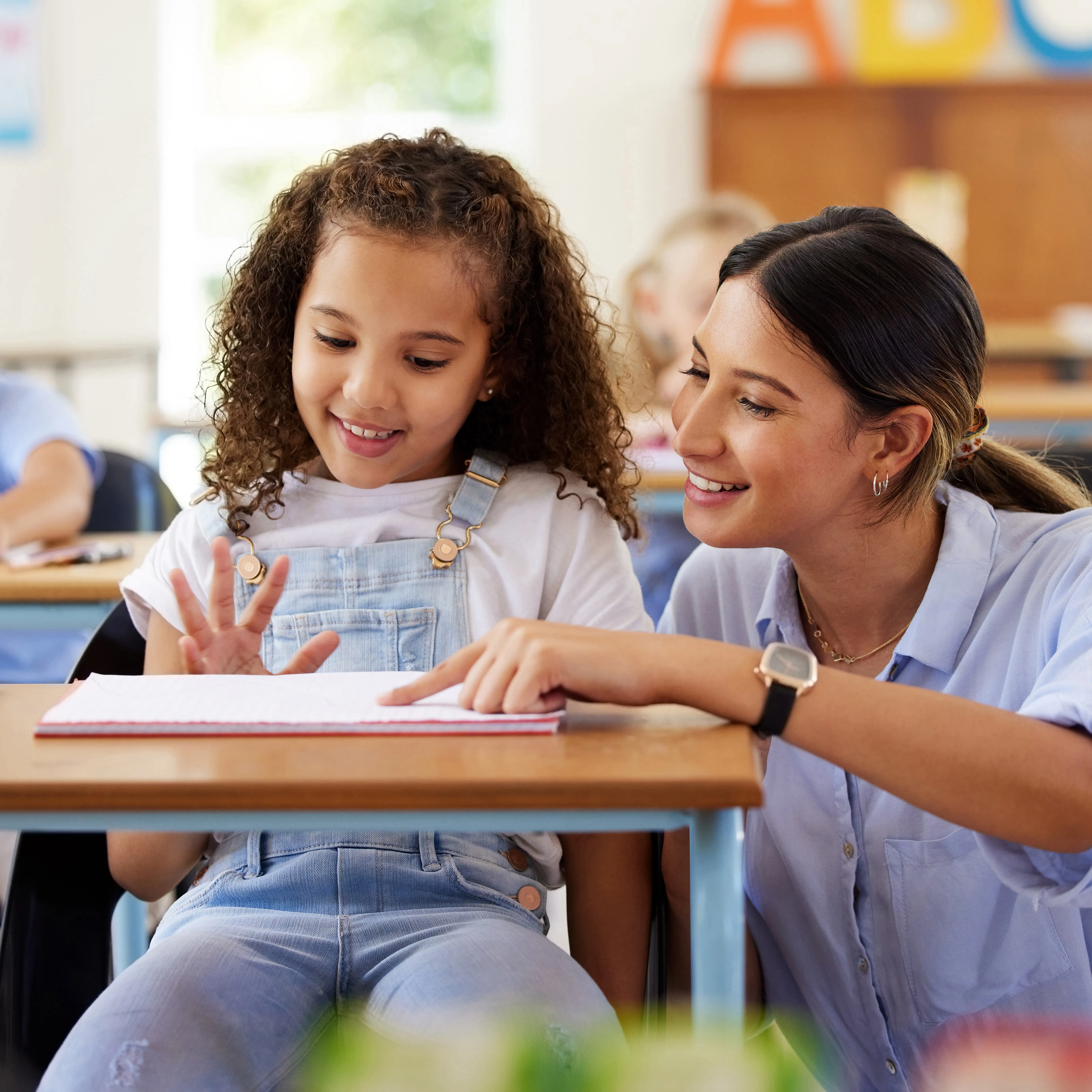 An educator assisting a student at her desk.