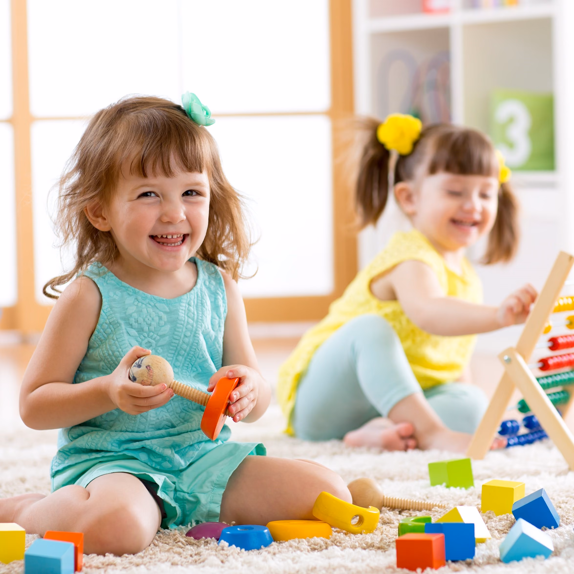 Two little girls playing with blocks and laughing.