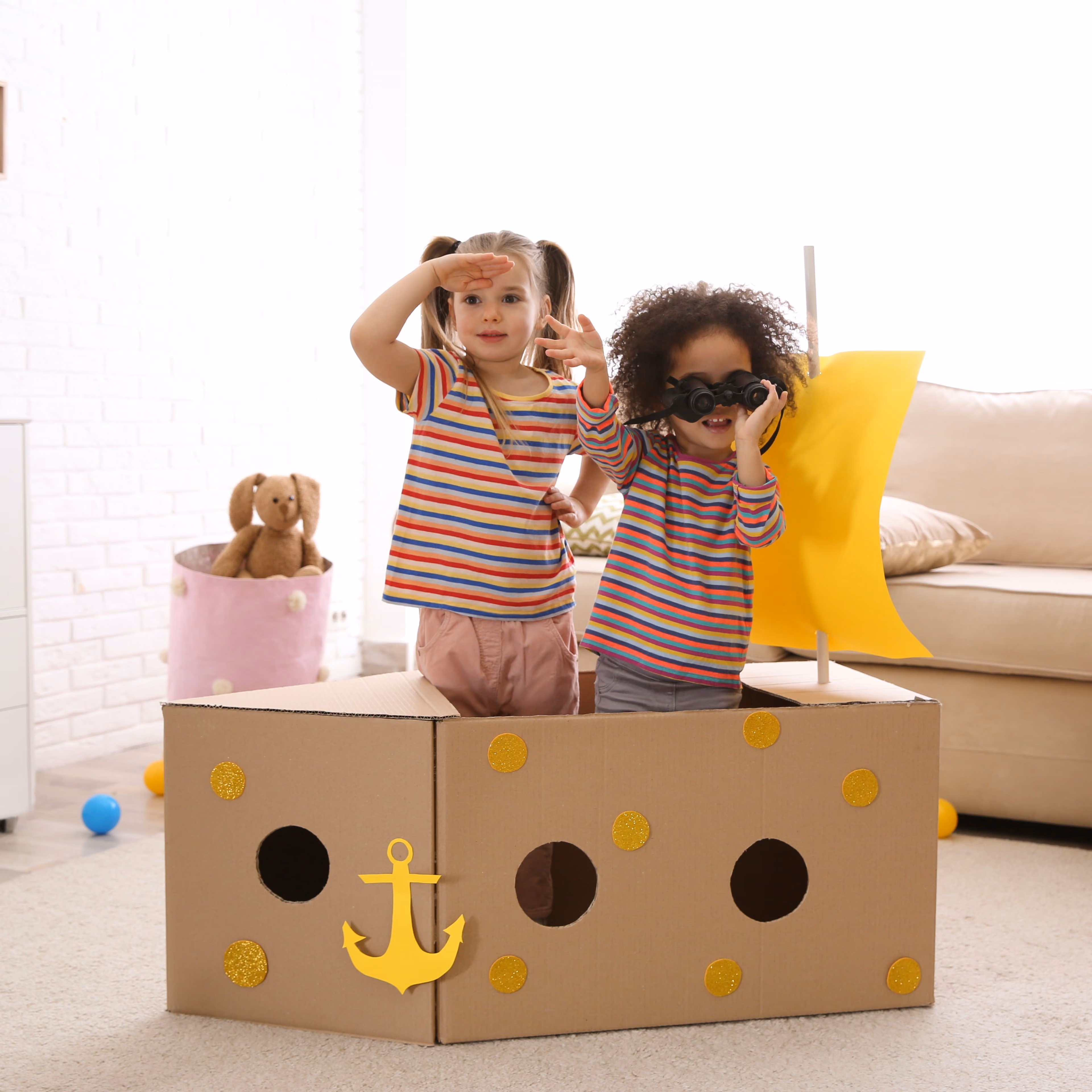 Two little girls playing pretend in a pirate ship made of boxes.