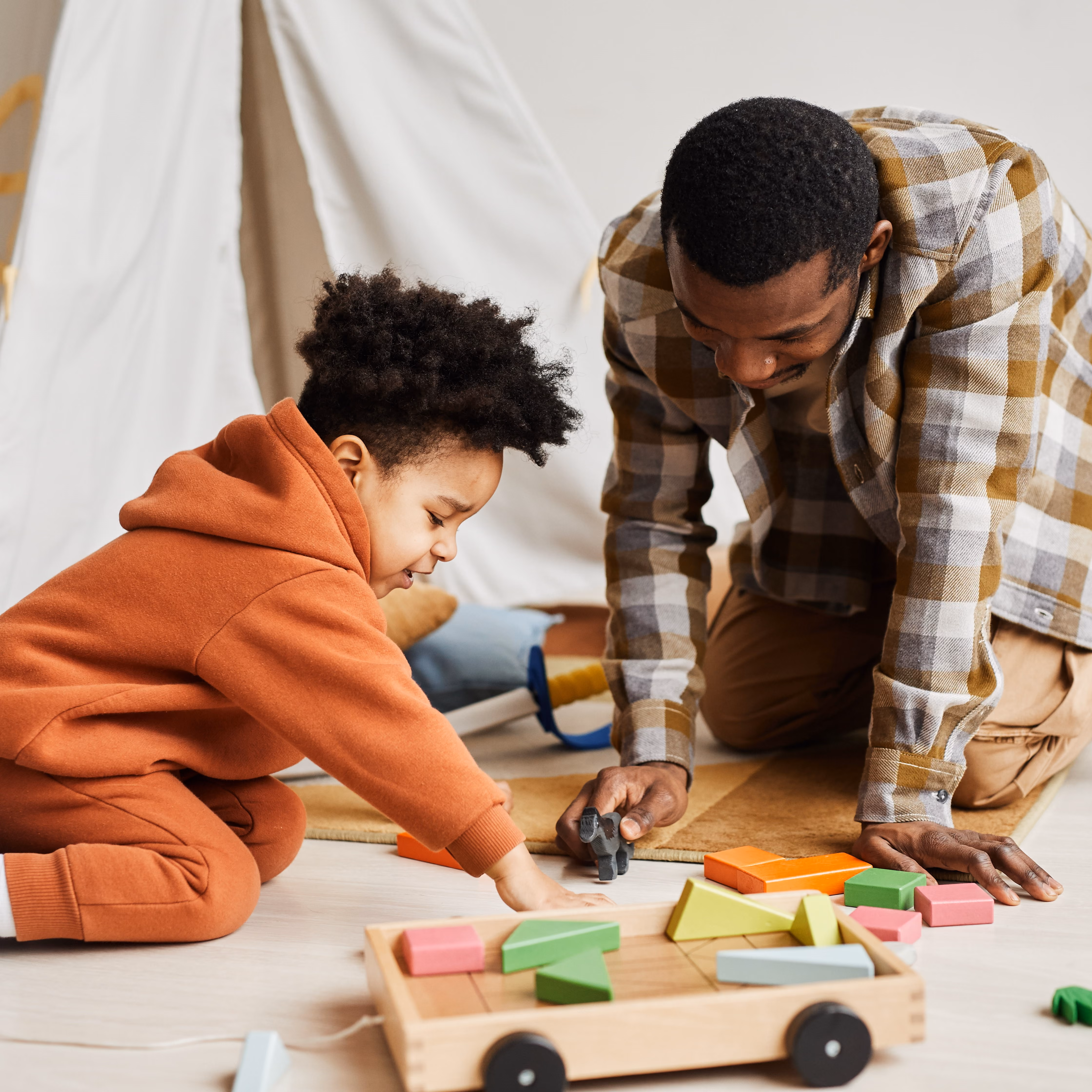 A father and son are playing with toys on the floor of their home.