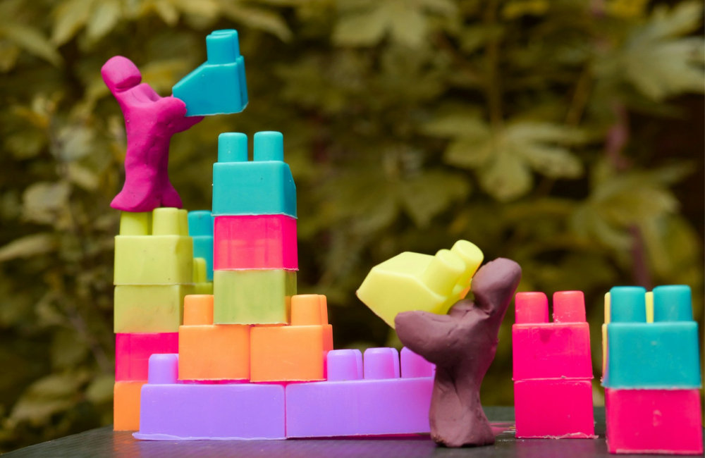 Plasticine people building with plastic connecting blocks.