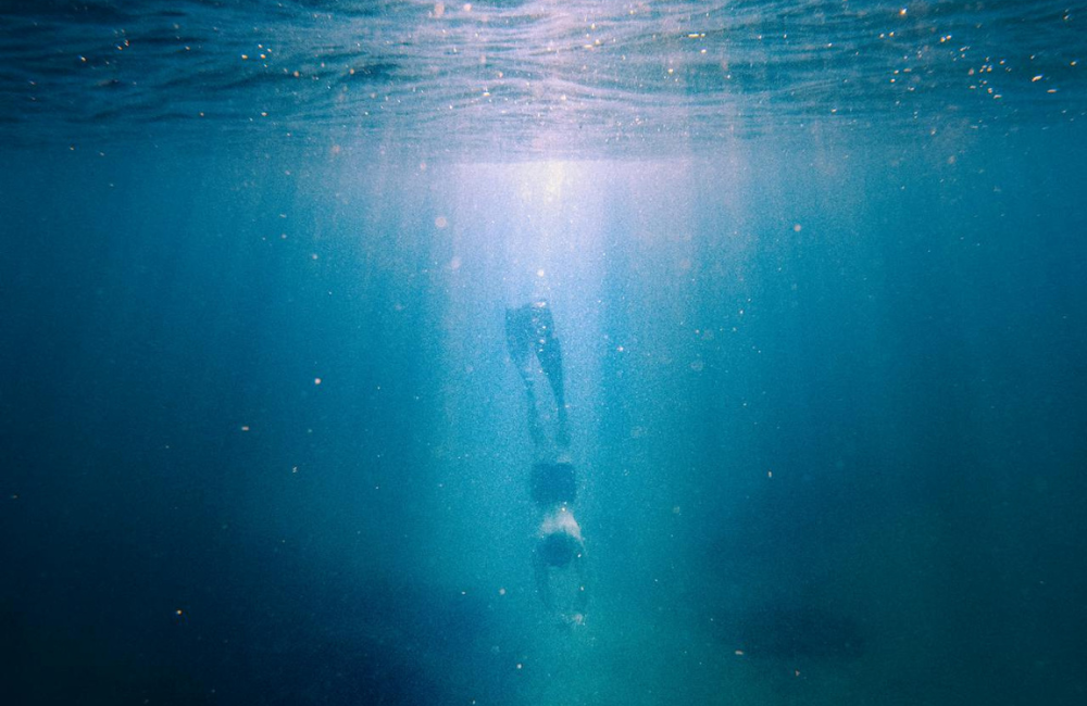 A person diving in water that has unclear visibility.