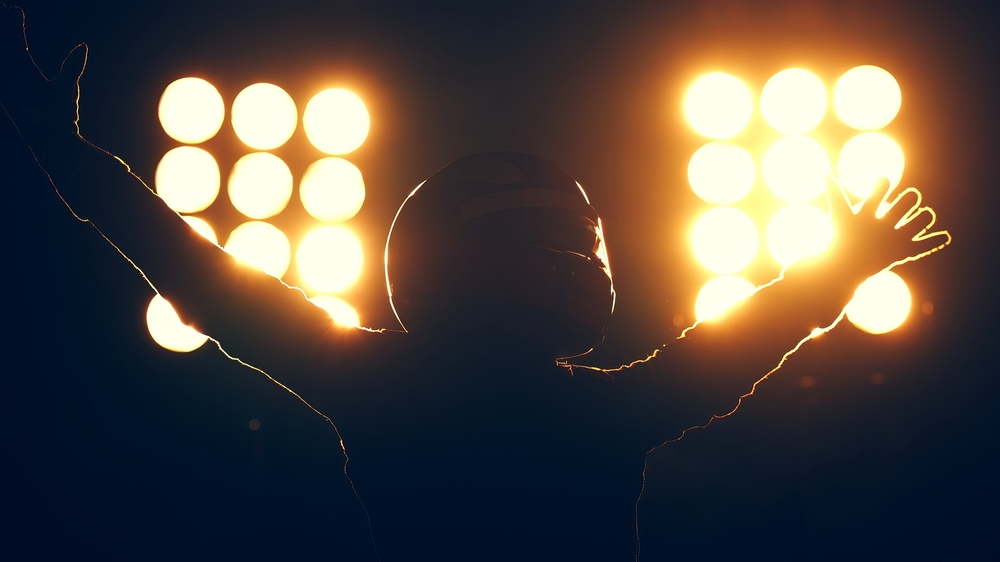 A motorcycle riding celebrating victory. They are silhouetted by the bright lights behind them.