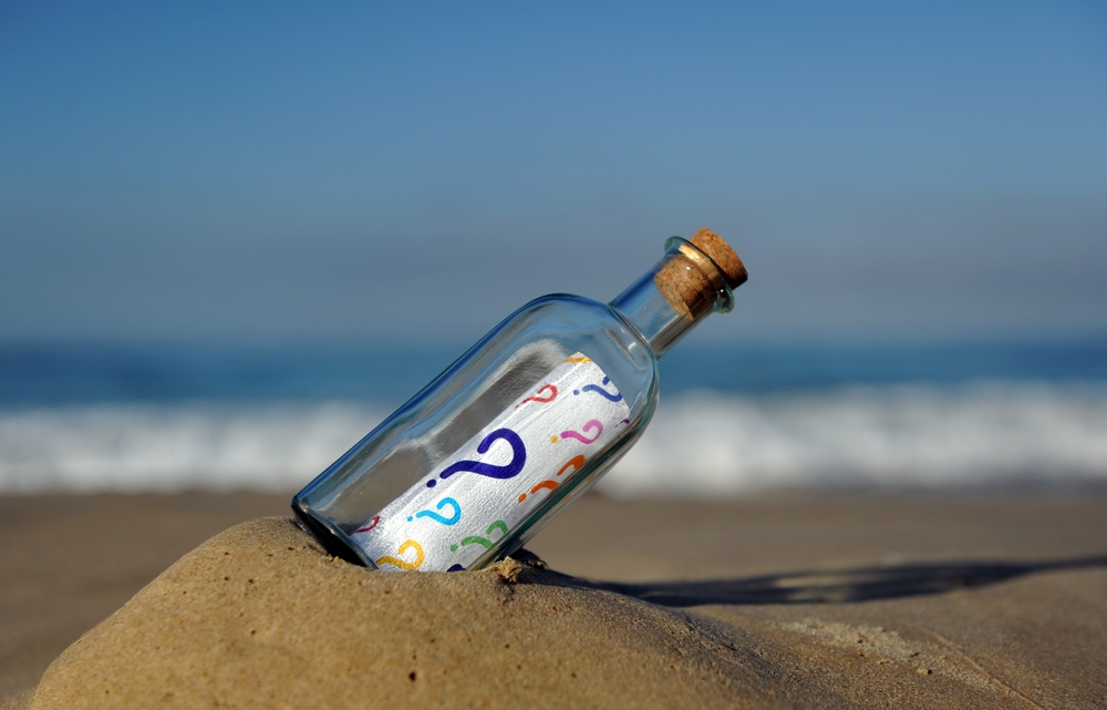 A piece of paper covered in question marks inside a bottle washed up on a beach.