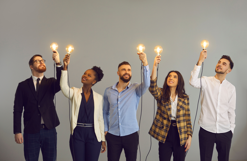 Five different people holding up a lit up lightbulb.