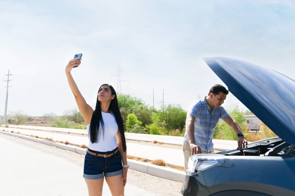 A woman checking reception on her phone while a man fixes the car. It is used as a metaphor for finding leverage with Reddit SEO to drive traffic.