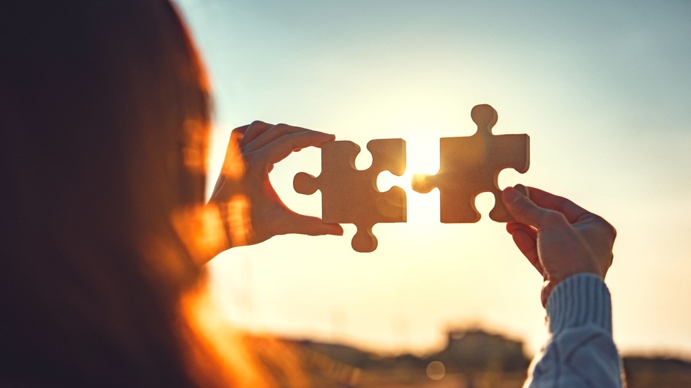 A person connecting two puzzle pieces together in the setting sun.