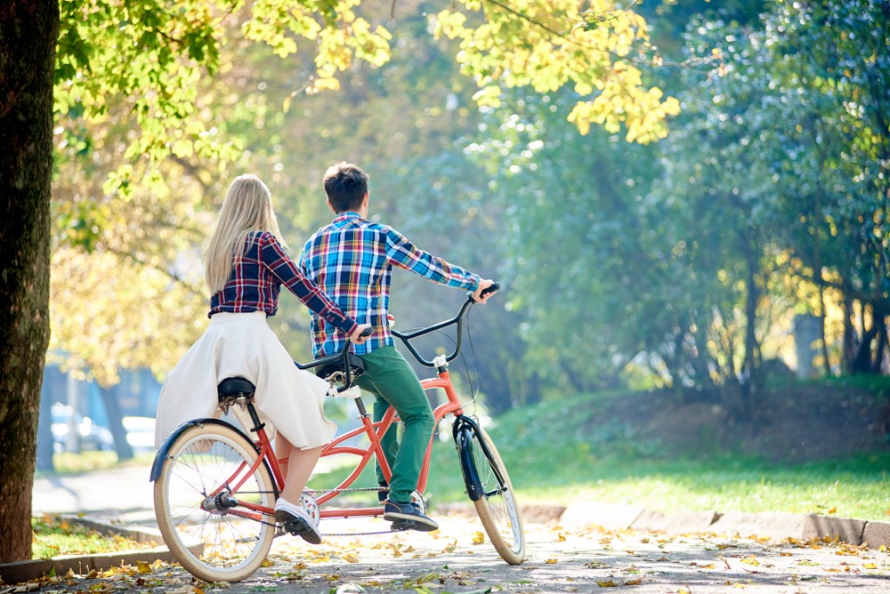 Two people working together riding a tandem bike in a park. 