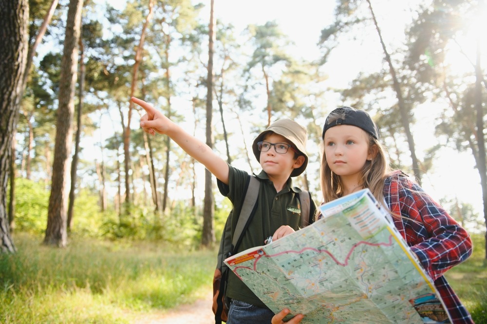 Two children in a forest. One is pointing and the other one is holding a map attempting to understand the search intent.