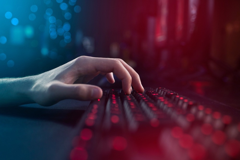 A hand on a keyboard with blue and red lighting around making it appear digital and modern.
