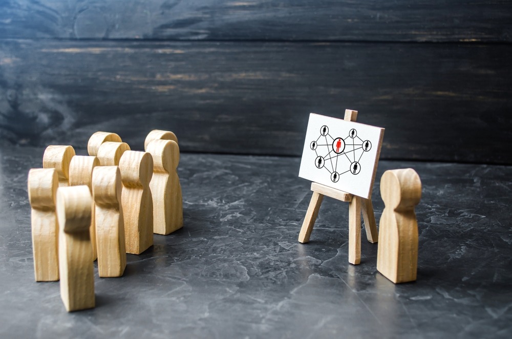Wooden figures looking at another wooden figure displaying a diagram of interconnectedness.